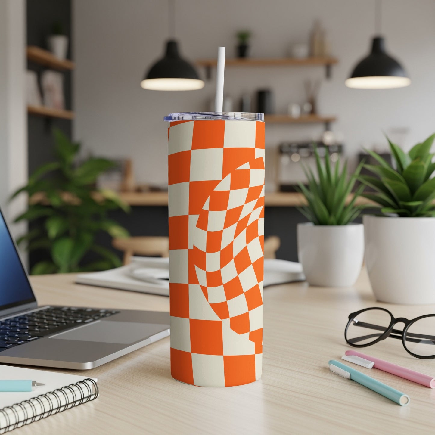 Orange and white checkered tumbler with straw on a desk.