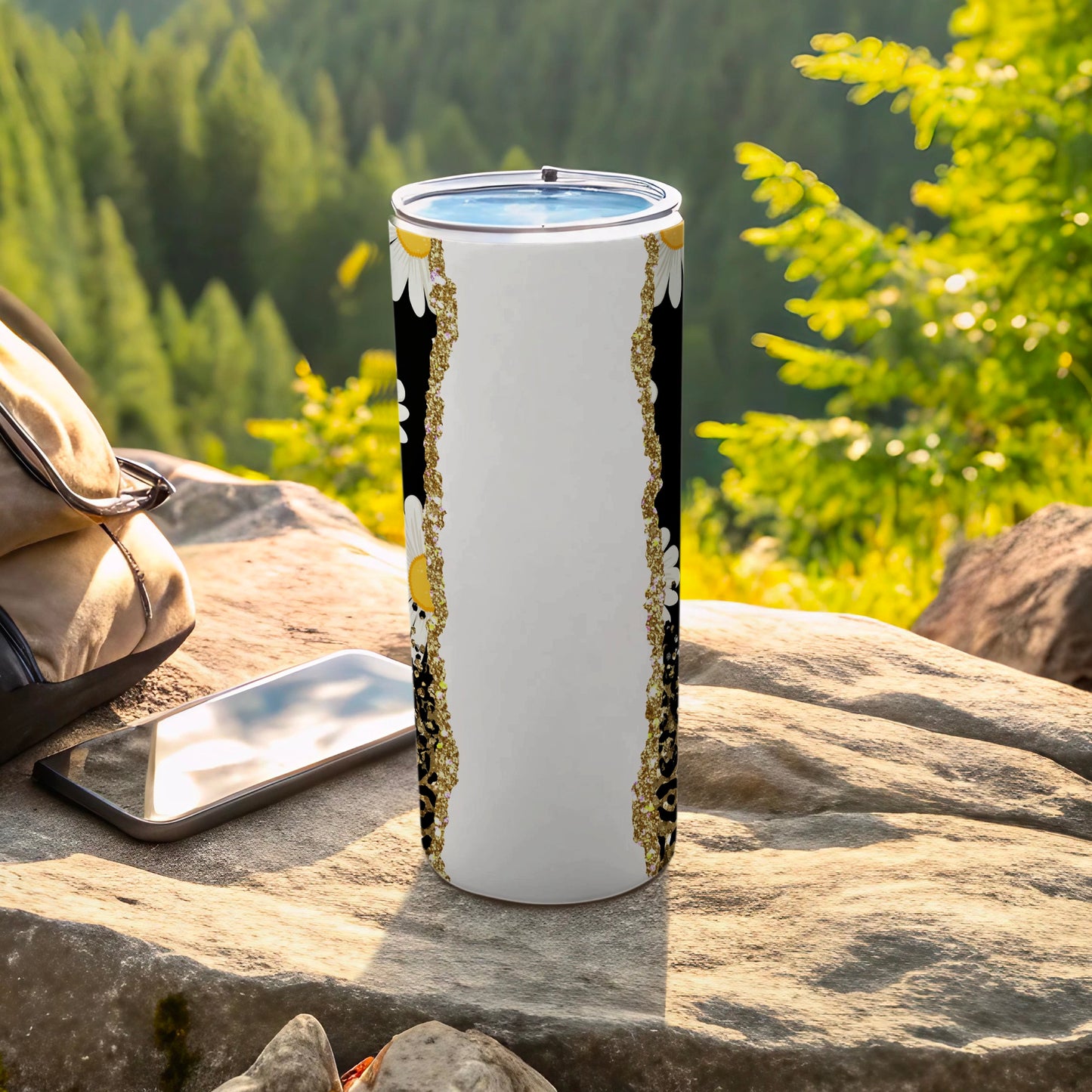 White tumbler with black and gold floral border on rocky surface.