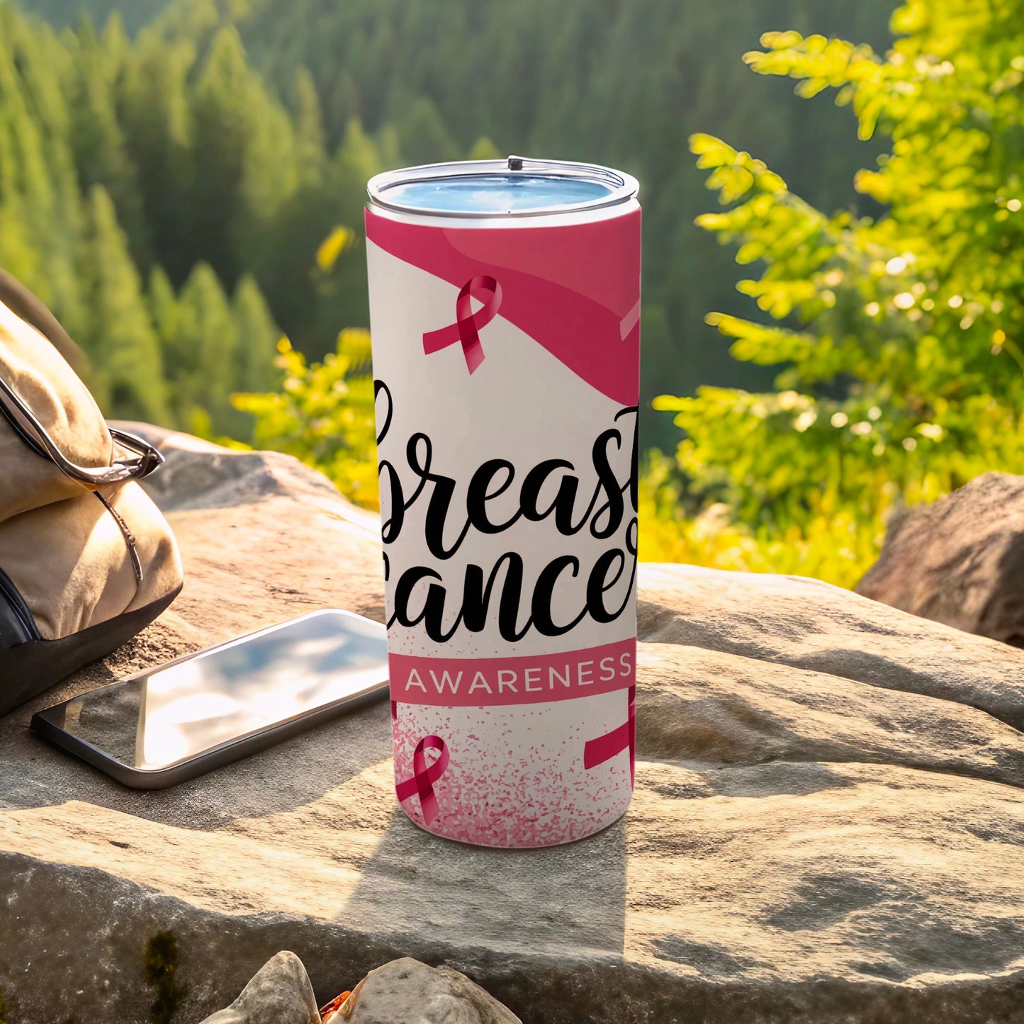 Pink ribbon breast cancer awareness tumbler with text on rocks.