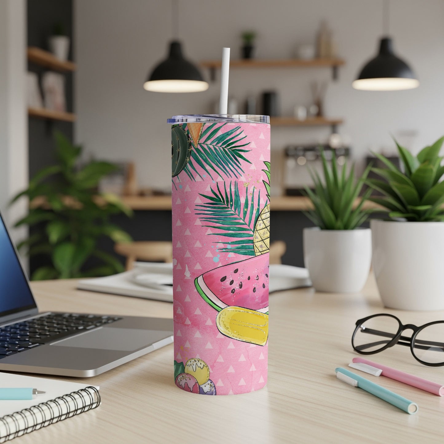 Pink tumbler with watermelon, pineapple, and palm leaf design on a desk.