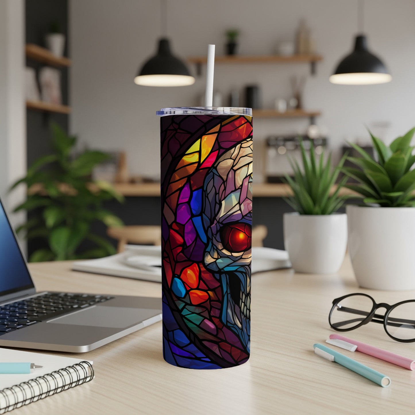 Stained glass skull tumbler with straw on a desk next to a laptop.