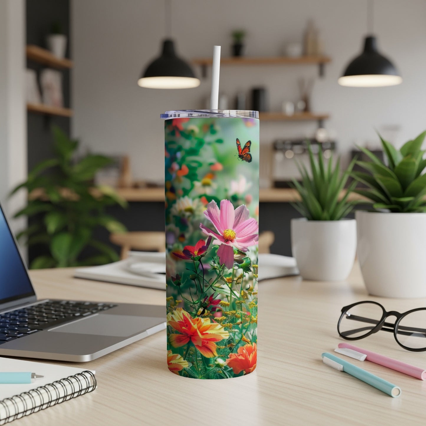 Floral design on a stainless steel tumbler with a straw, set on a desk.