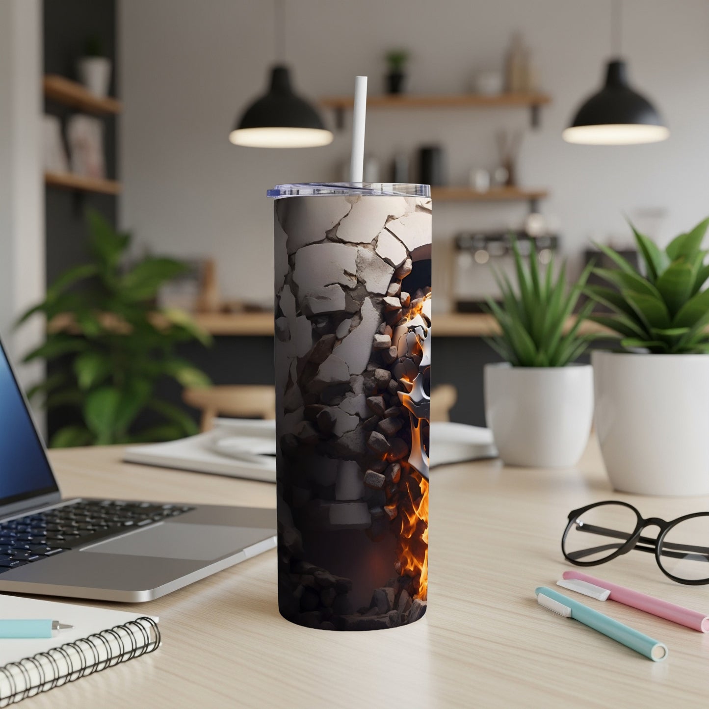 Tumbler with broken concrete and fire graphic, on a desk with laptop and notebook.