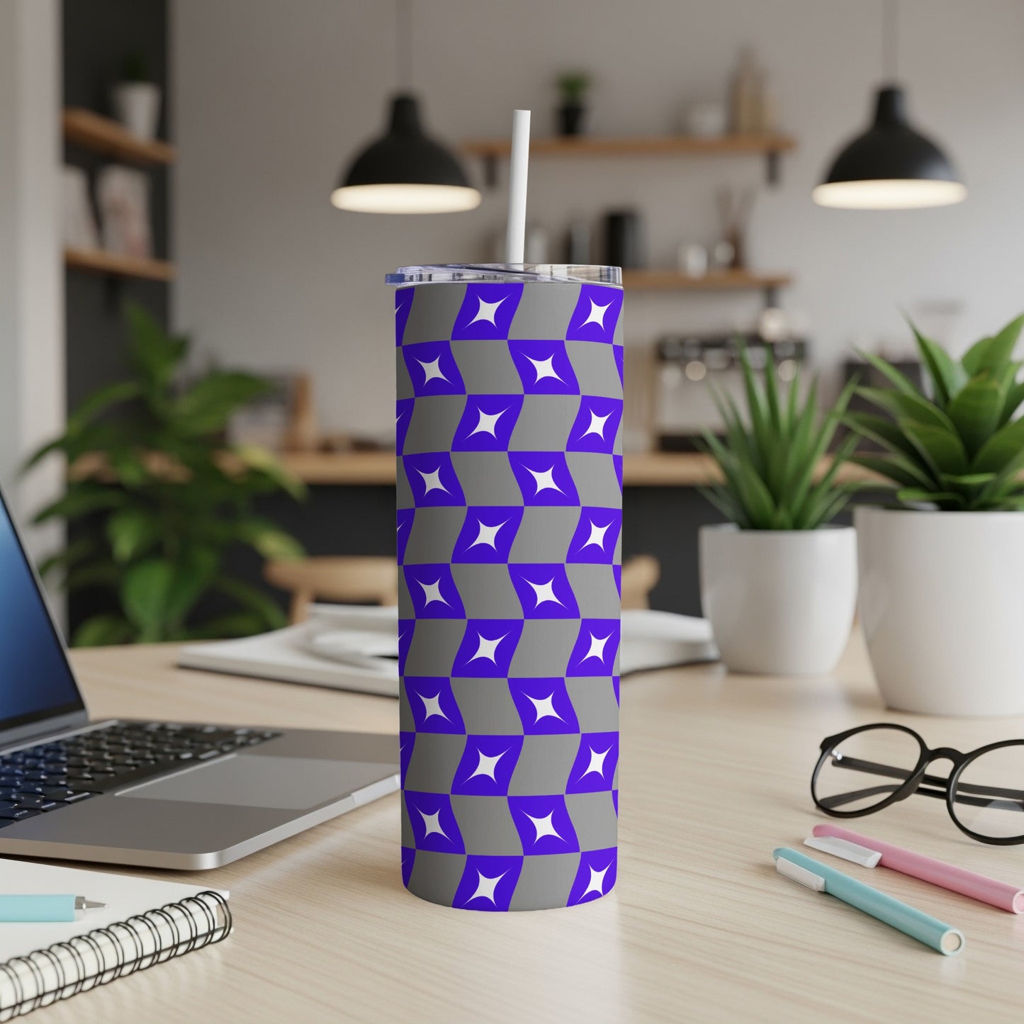 Gray tumbler with purple starburst pattern on desk with laptop and pens.