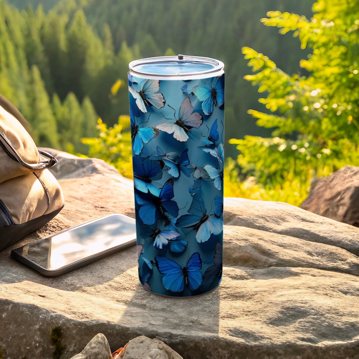 Blue butterfly patterned tumbler on a rock next to a backpack and phone.