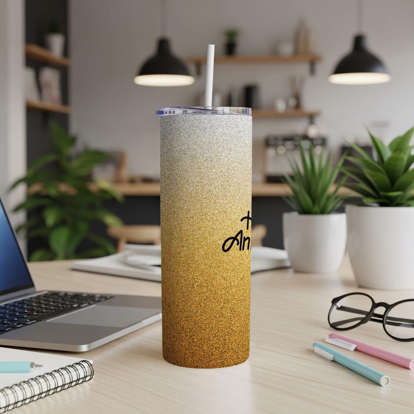 Glittery gold tumbler with "+ Am" text on a desk with a laptop.