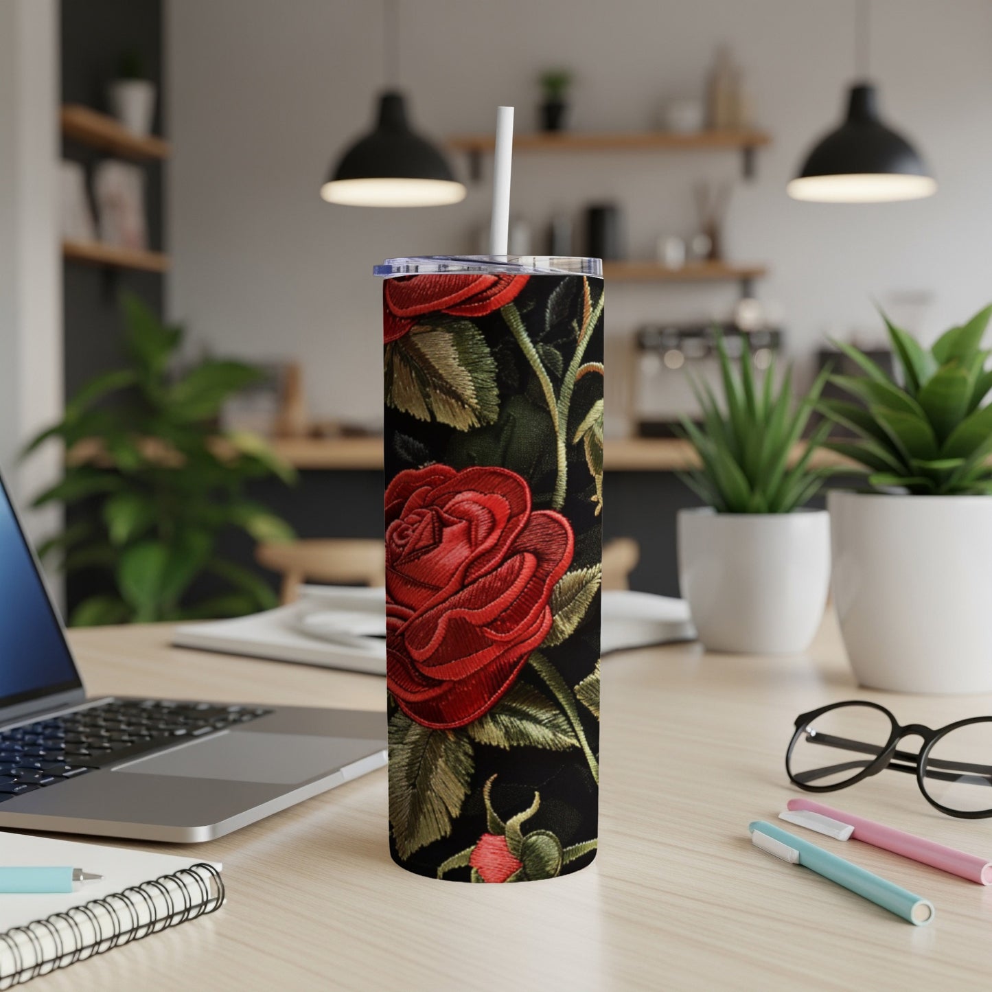 Red rose embroidered black tumbler with straw on a desk.