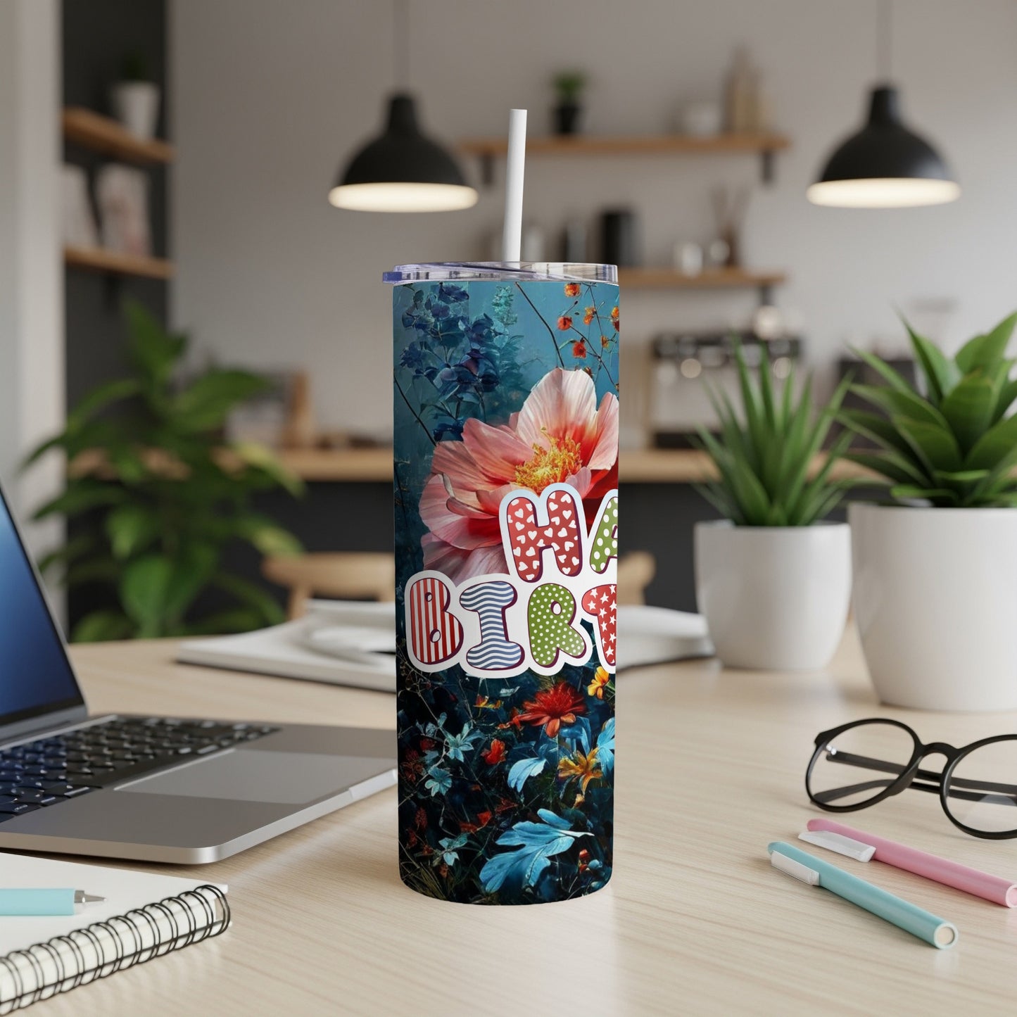 "Birthday" text on a floral tumbler with a straw, on a desk.