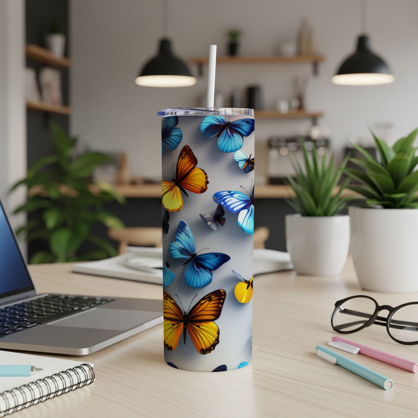 White tumbler with colorful butterflies, on a desk with laptop and pens.