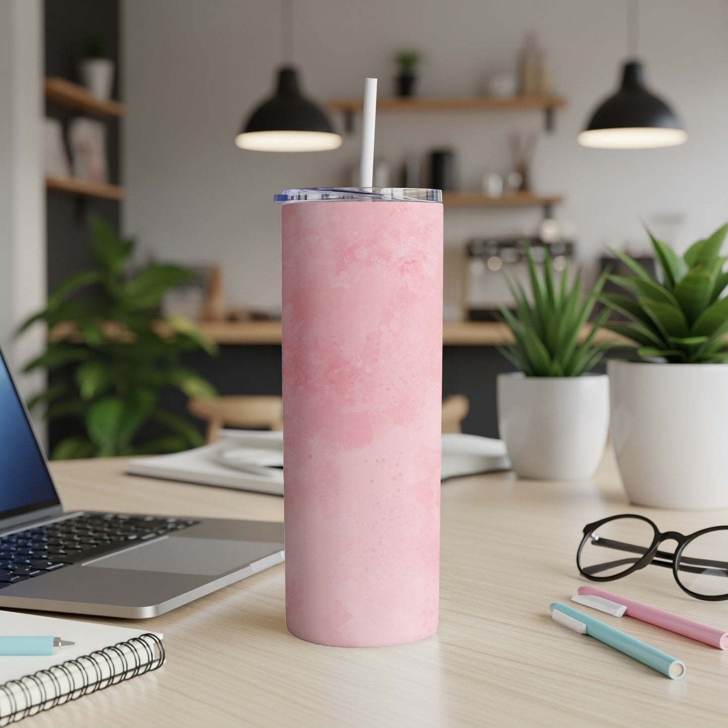 Pink marbled tumbler with straw on a desk next to a laptop and pens.