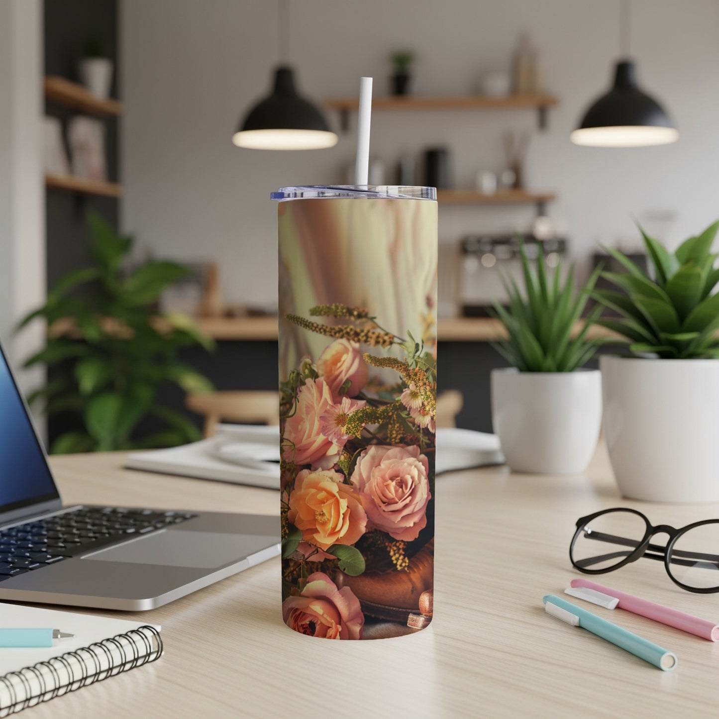 Floral pattern tumbler with roses and a straw on a desk.