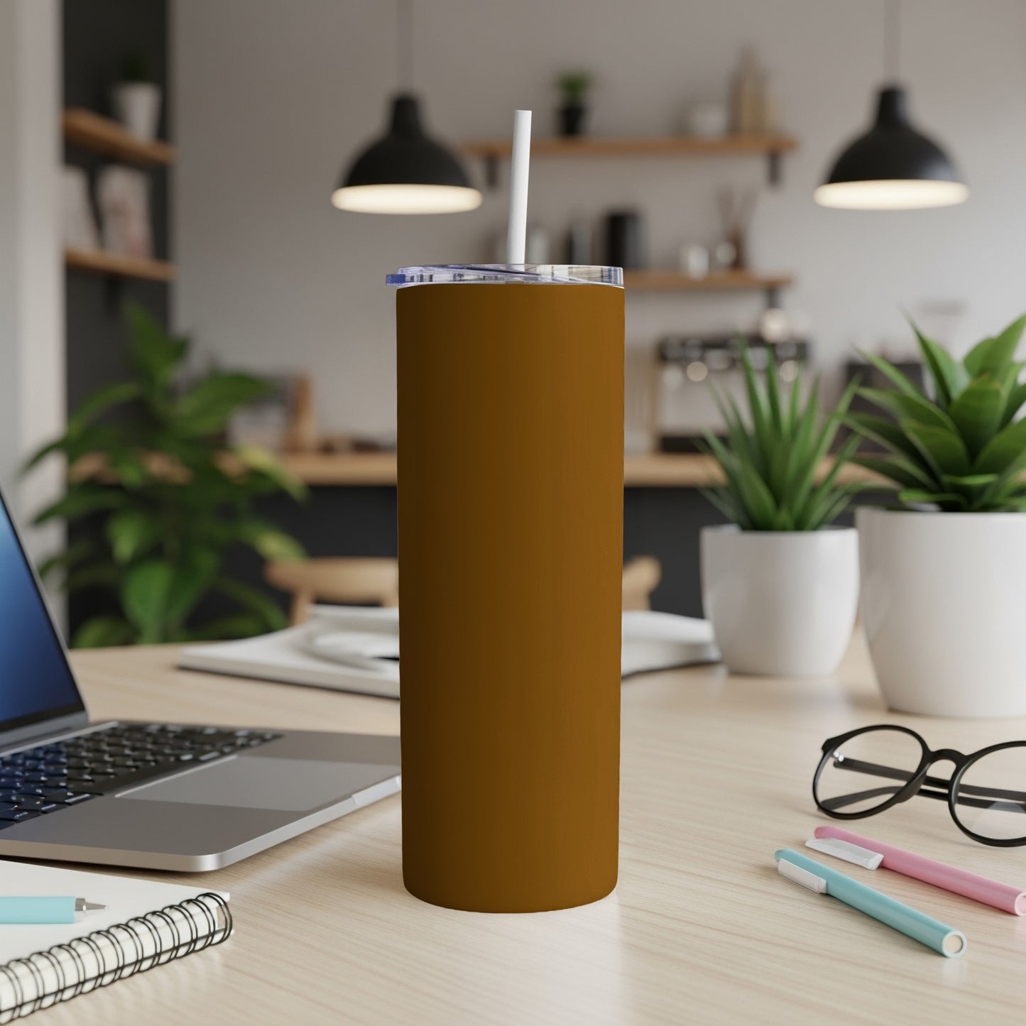 Brown tumbler with straw on desk next to laptop and pens.
