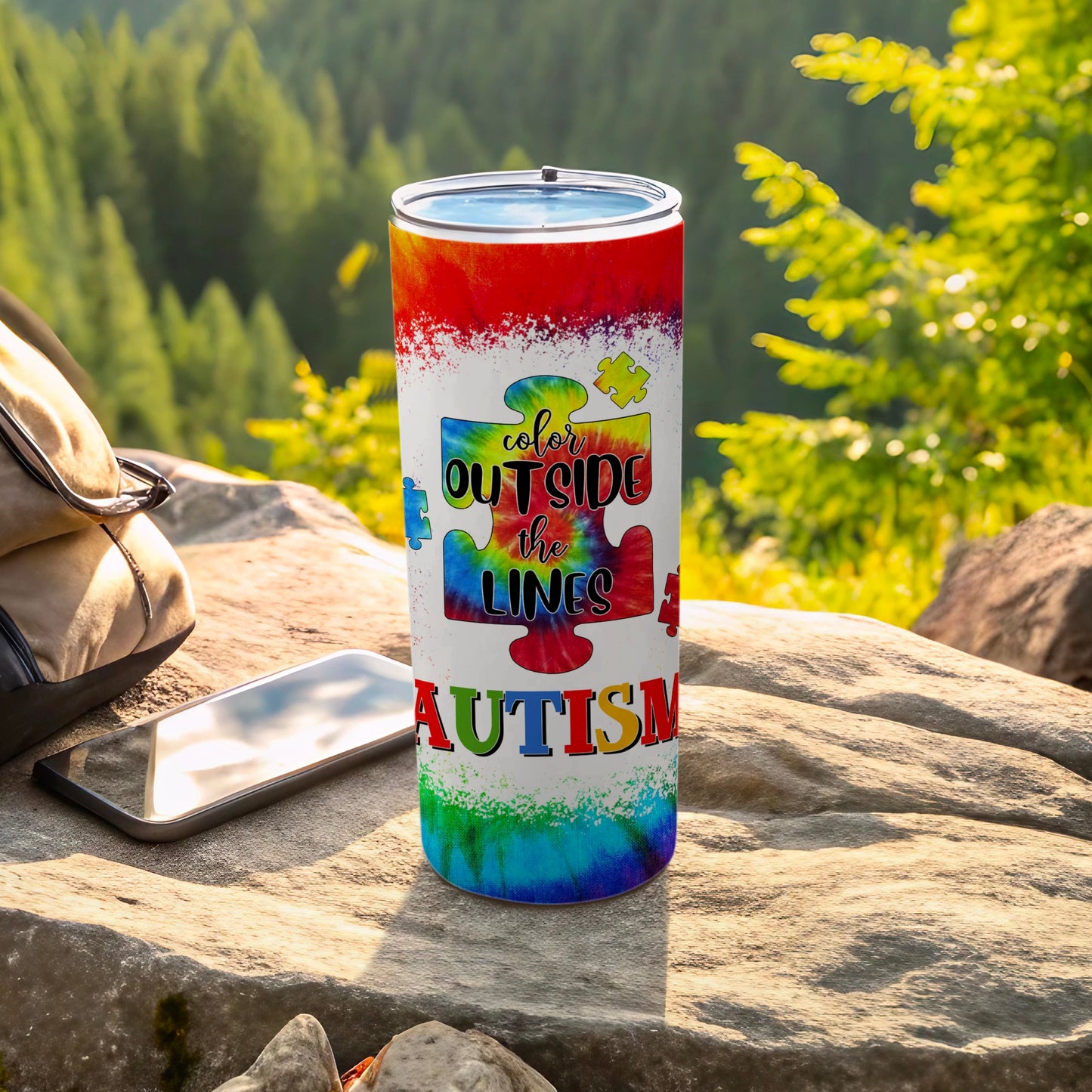 Tie-dye tumbler with "color outside the lines autism" text on a rock.