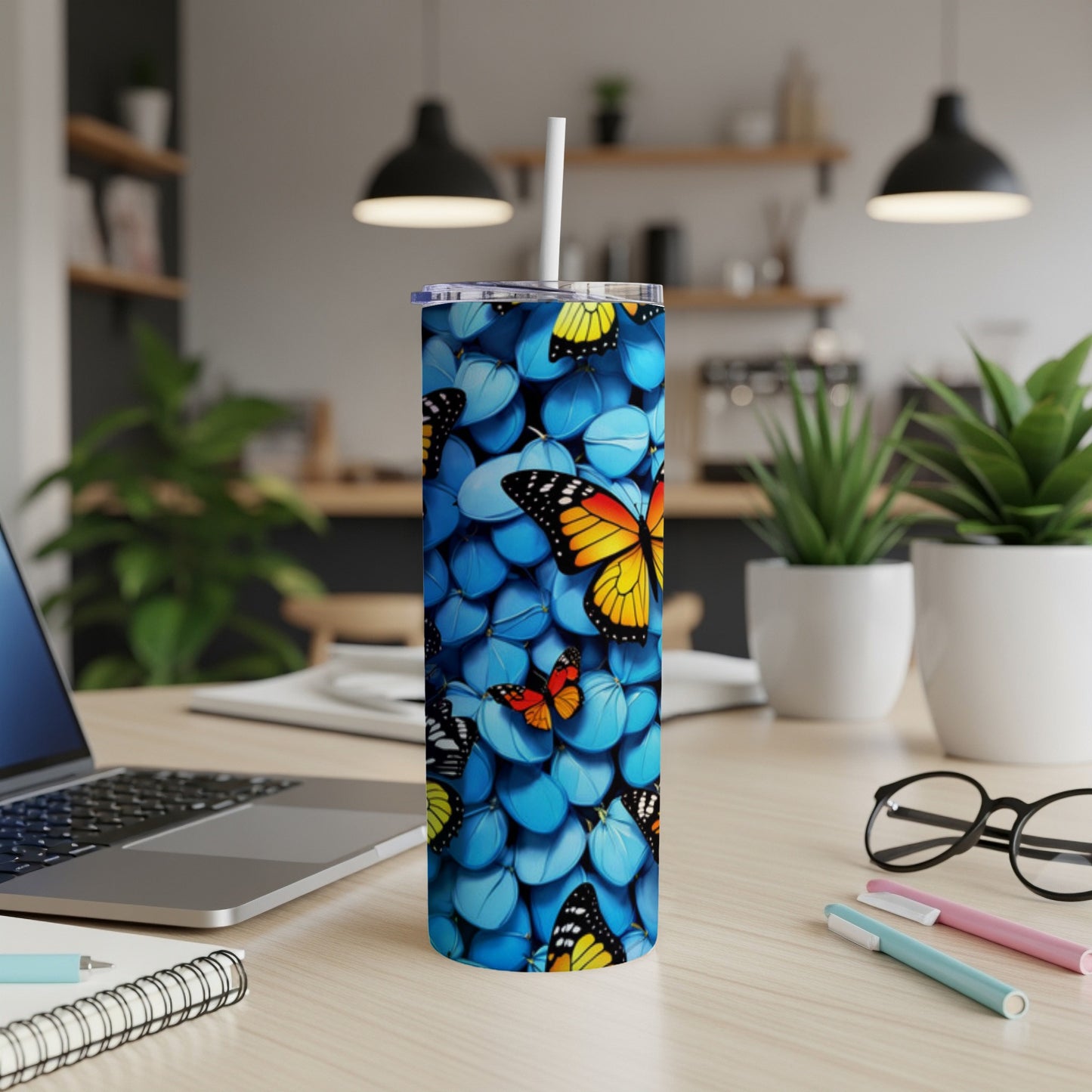 Blue tumbler with butterfly pattern on a desk with laptop.