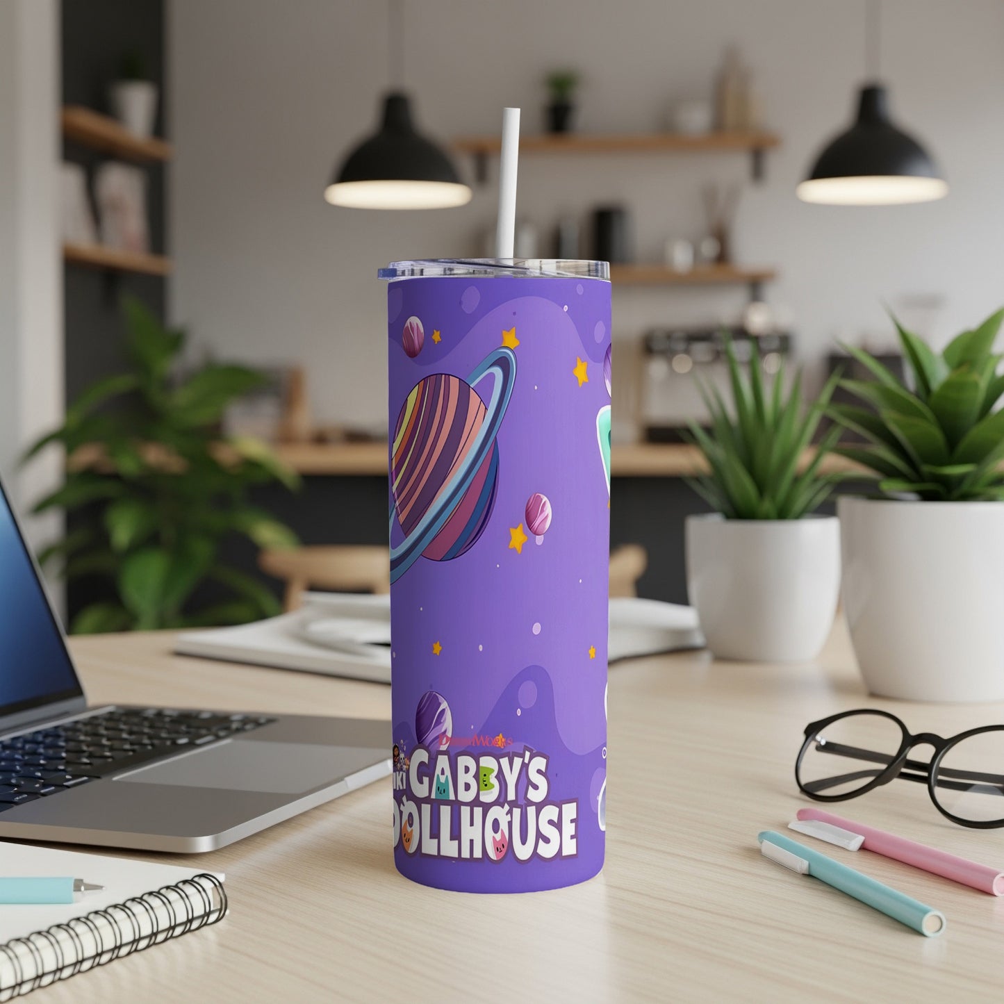 Purple tumbler with Gabby's Dollhouse characters and planets, on a desk.