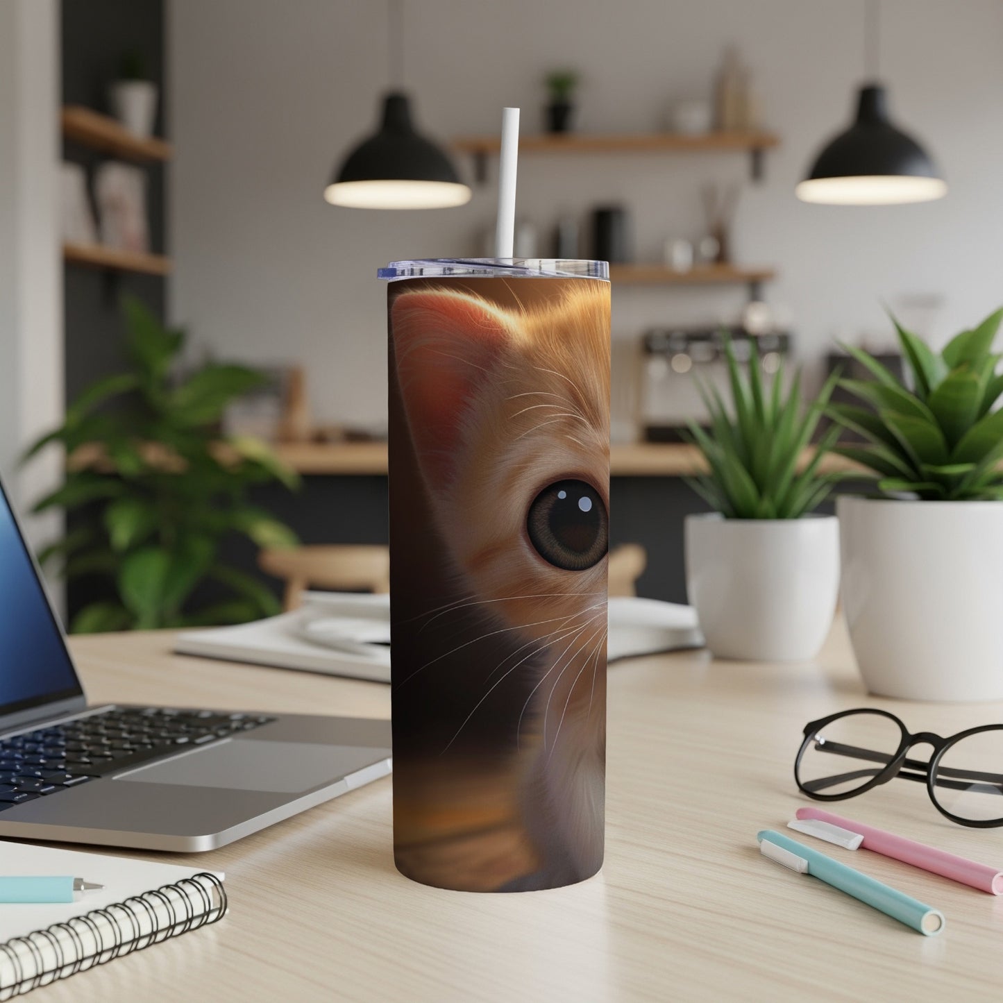 Orange tabby kitten peeking over a tumbler on a desk.