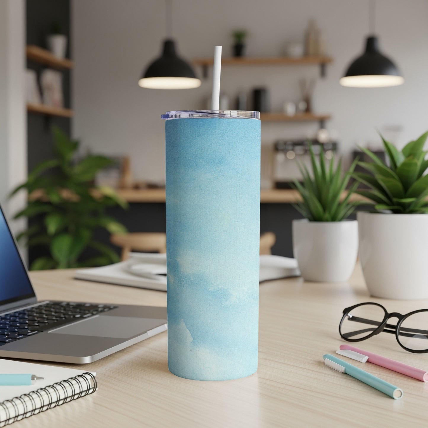 Blue watercolor sky design tumbler with straw on a desk.