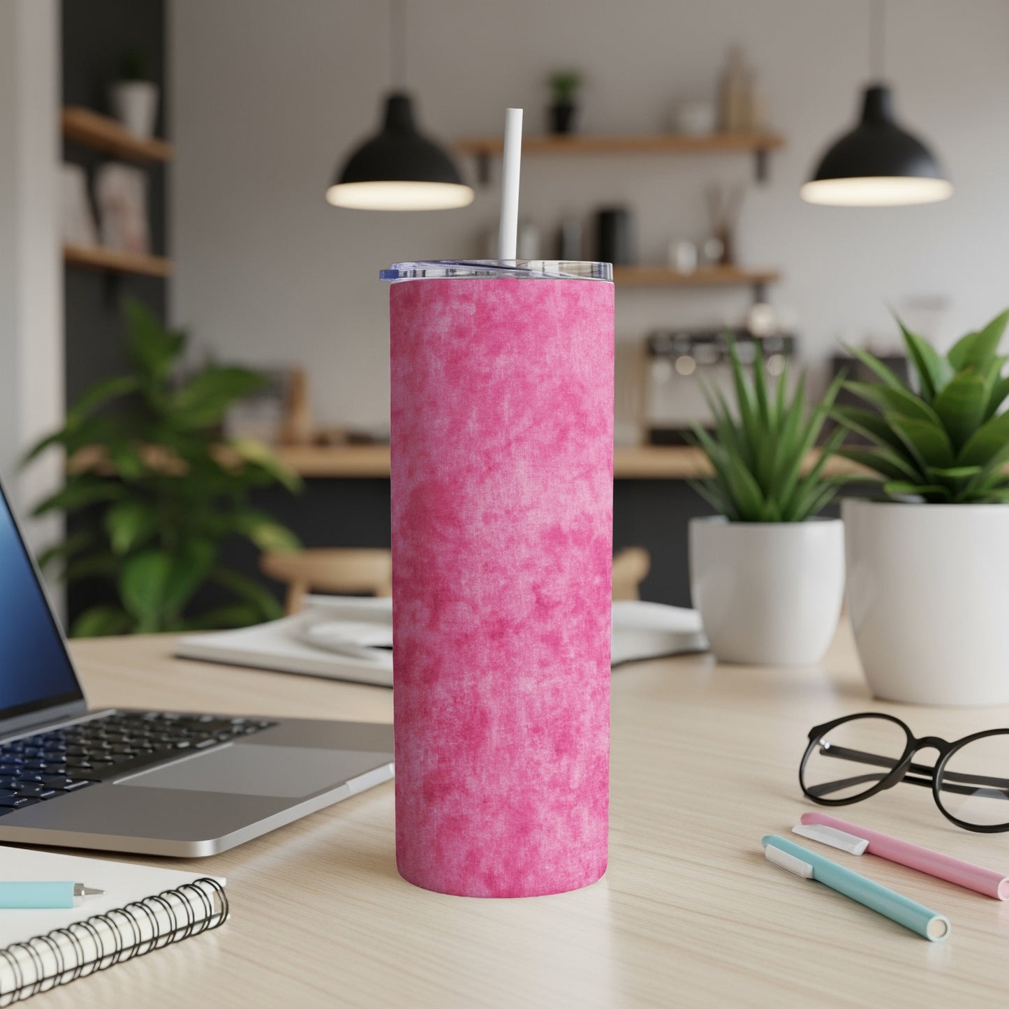 Pink marbled tumbler with straw on a desk next to a laptop and notebook.