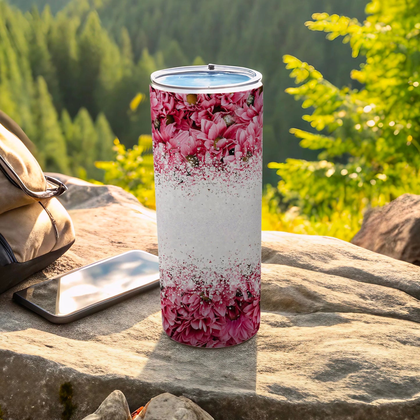 Floral tumbler on rock with backpack and phone.