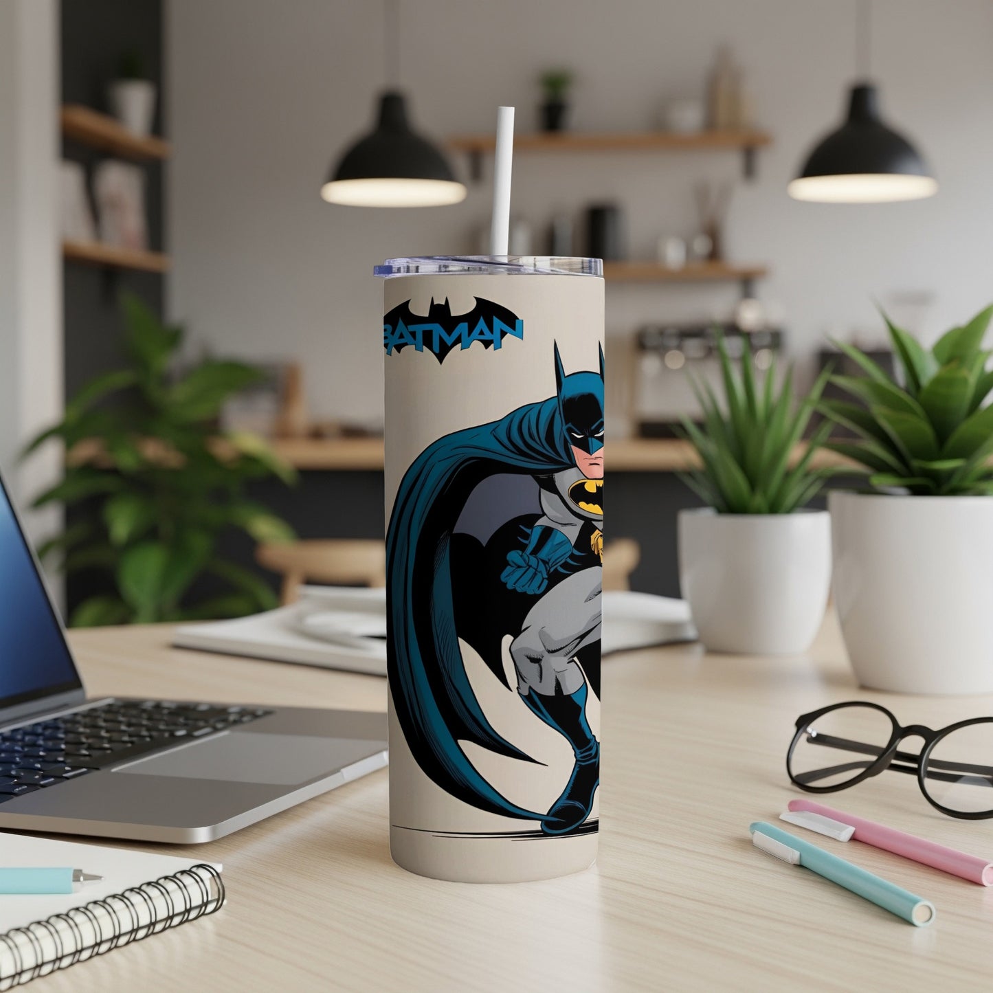 Batman tumbler with straw on a desk next to a laptop.