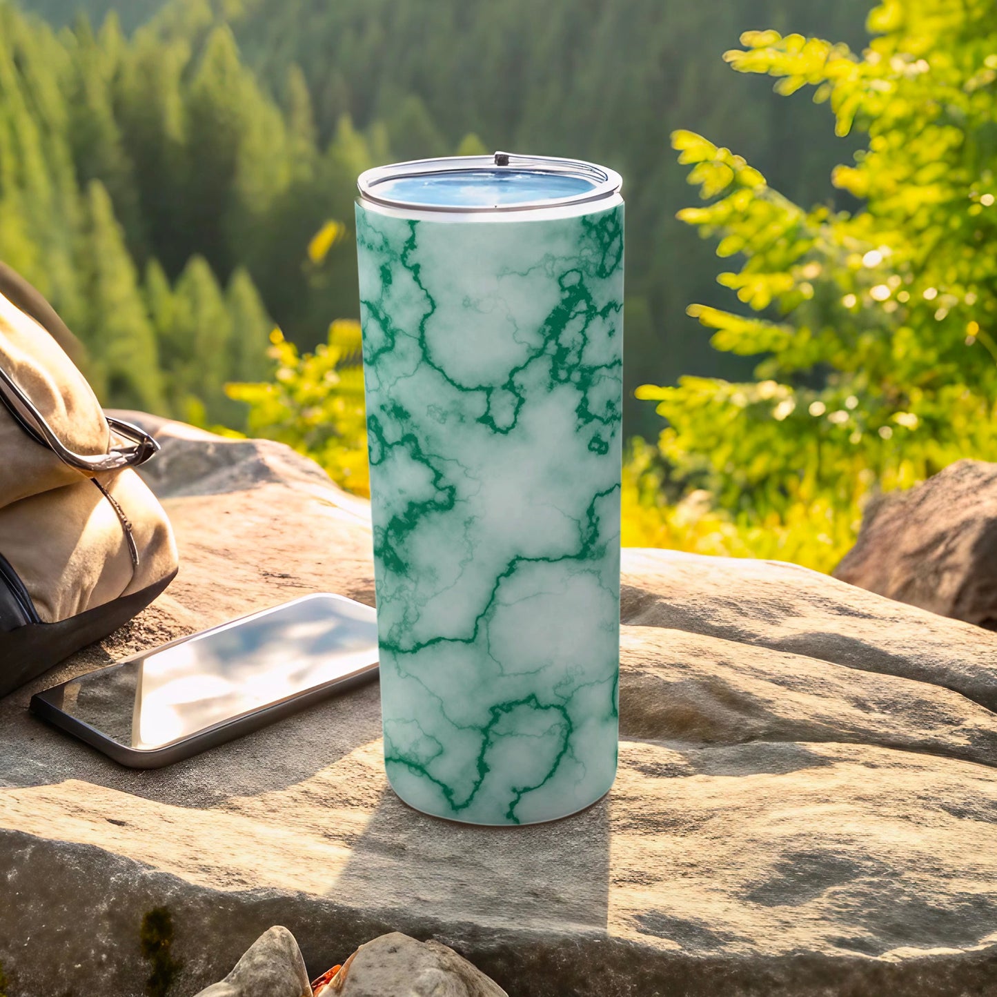 Green marble print tumbler on a rock with a phone and backpack.