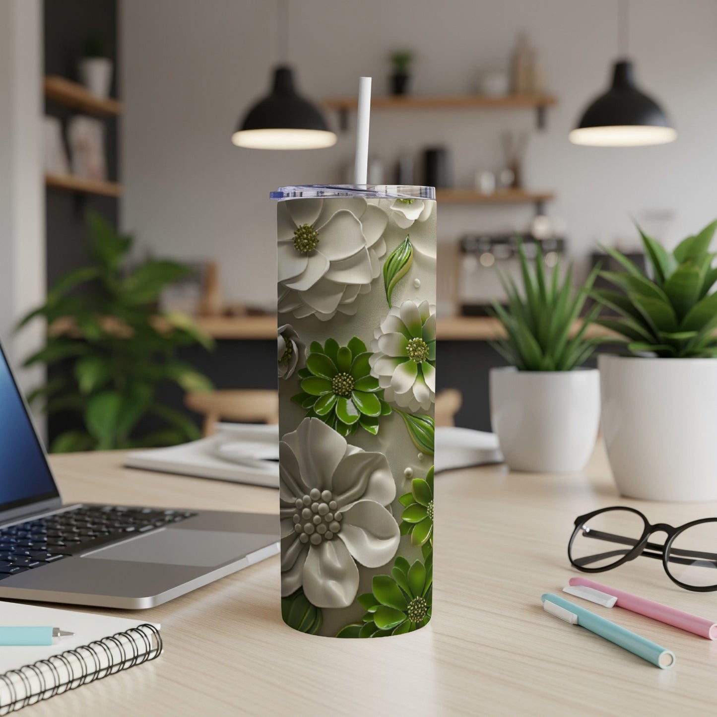 Floral embossed green and white tumbler with straw on desk.