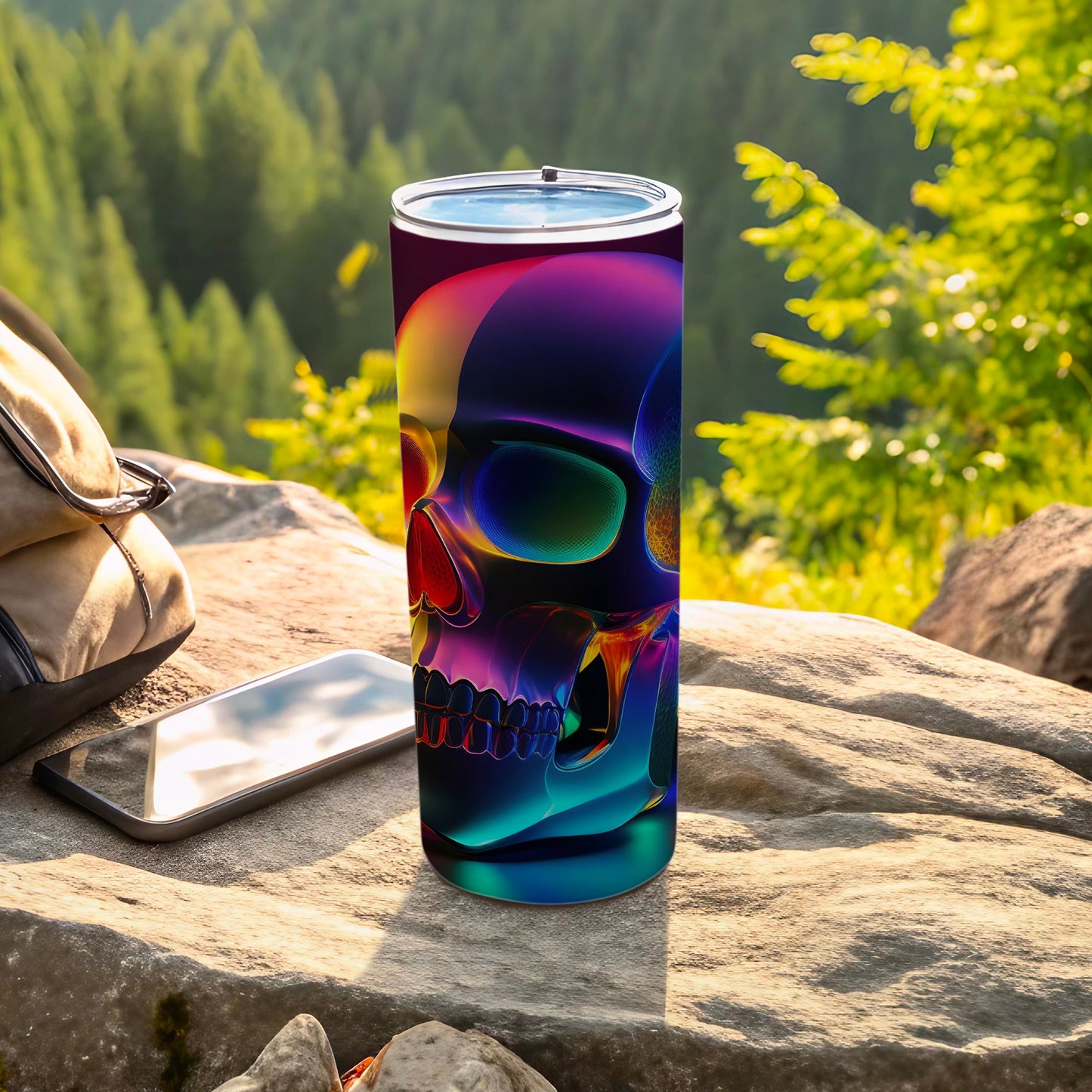 Colorful iridescent skull tumbler resting on rocks with phone and backpack.