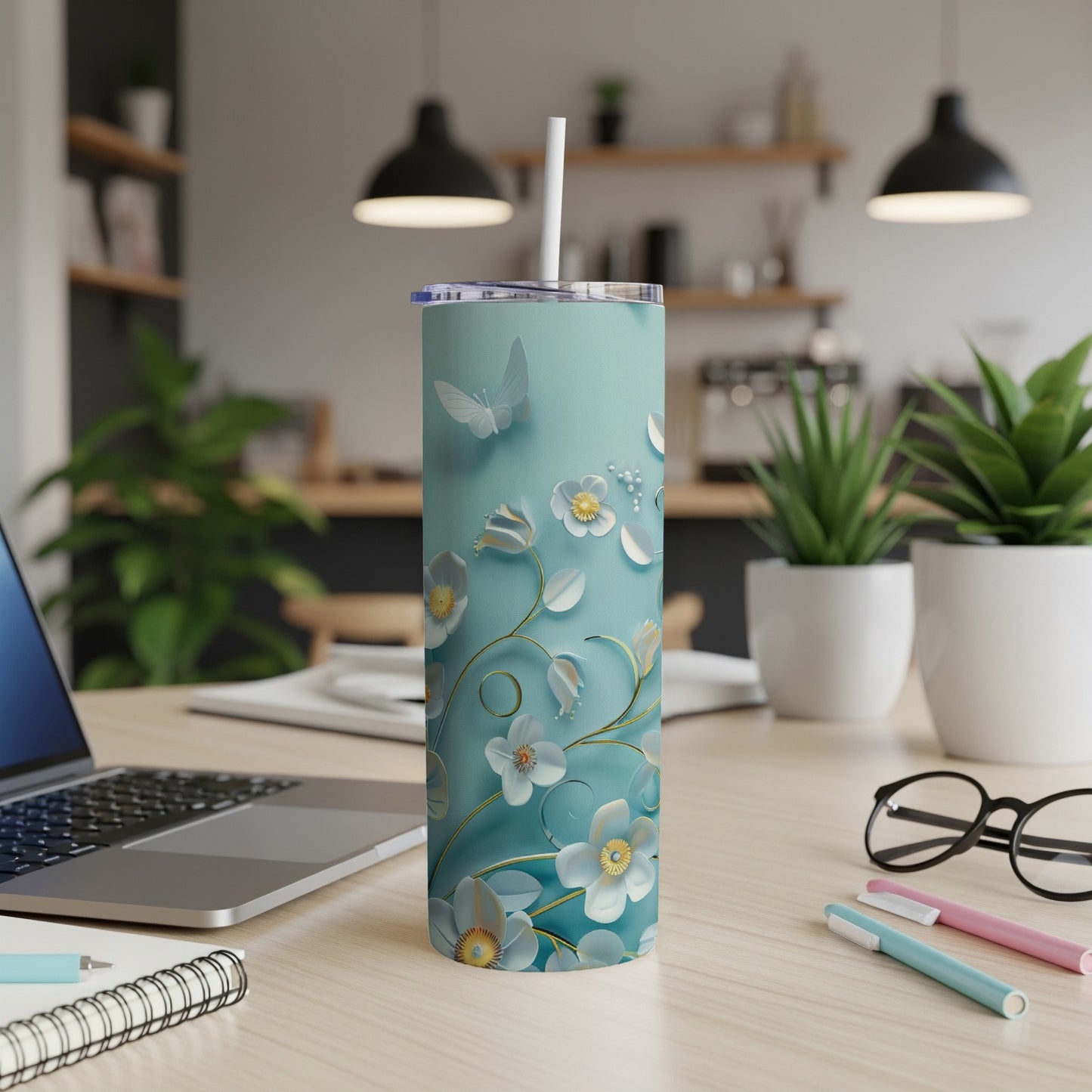 Teal tumbler with floral design and straw on a wooden desk.