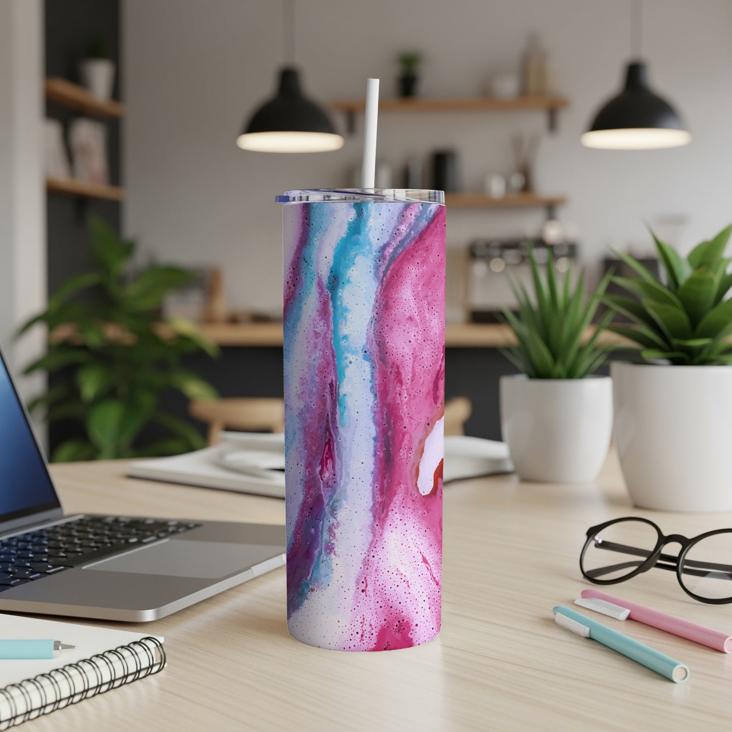 Tumbler with pink, blue, and white marbled design and a white straw on a wooden desk.