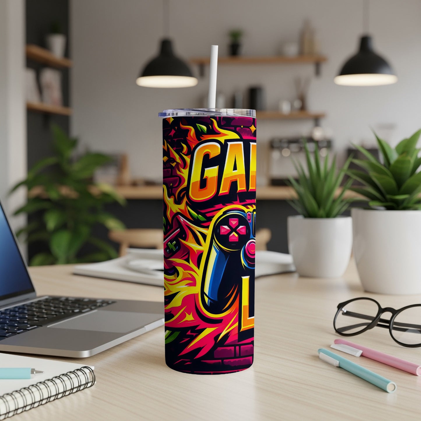 Gaming-themed tumbler with controller and graffiti, on a desk.