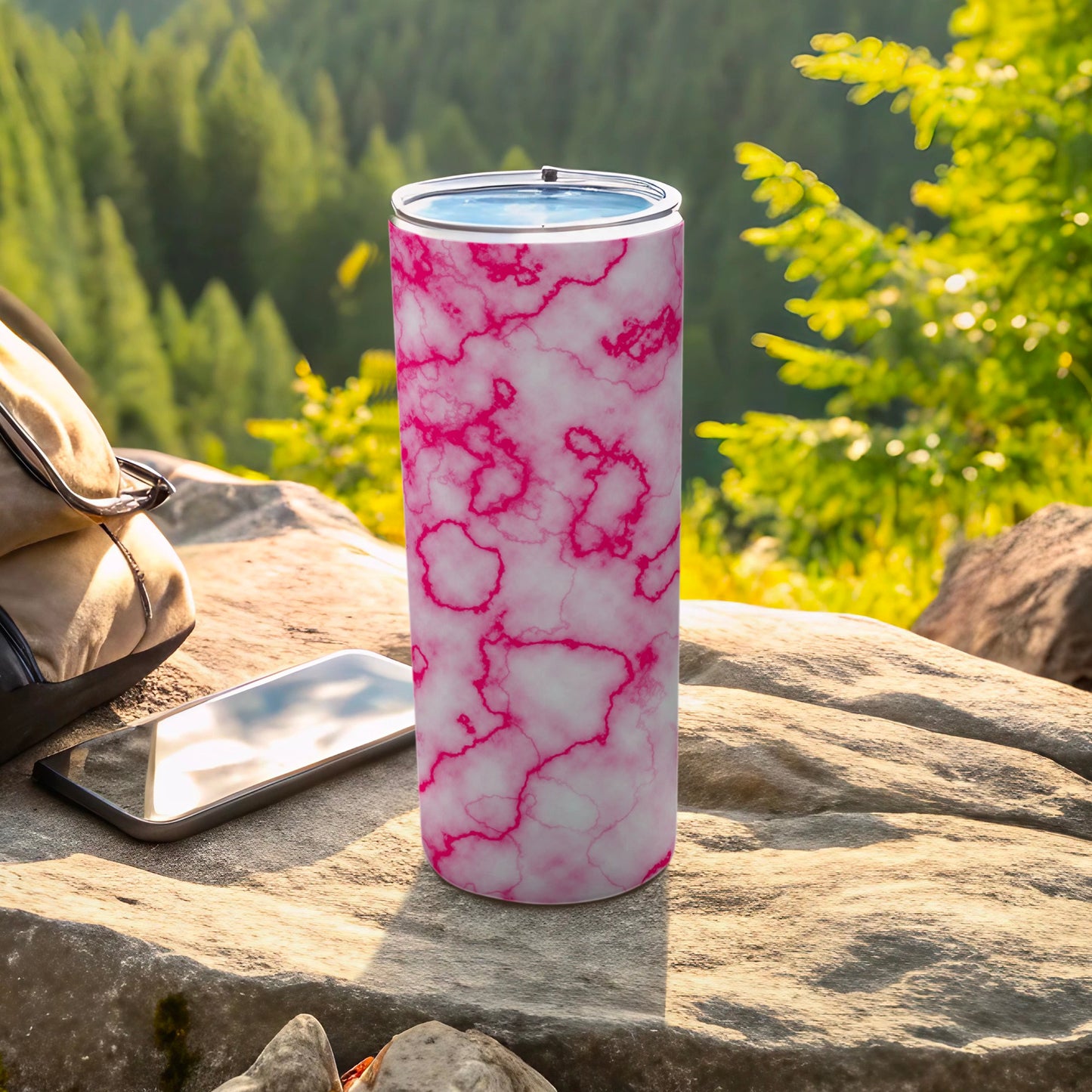 Pink marble pattern tumbler on rocks with phone and backpack.
