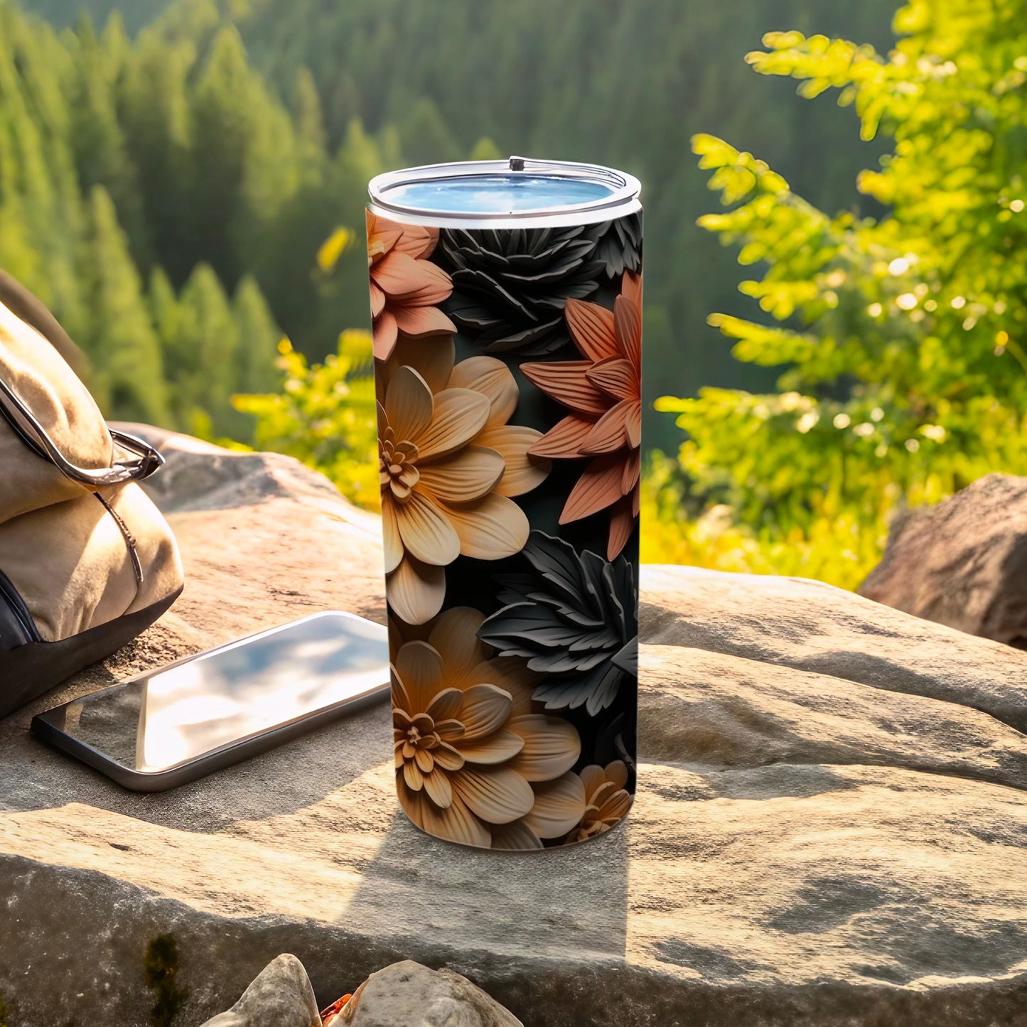 Tall floral tumbler on a rock next to a phone and bag.