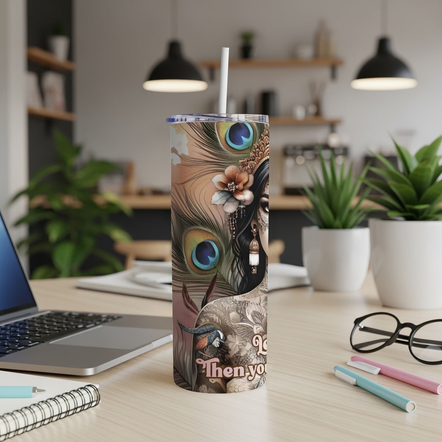 Peacock feather design on a white tumbler with a straw, on a desk.