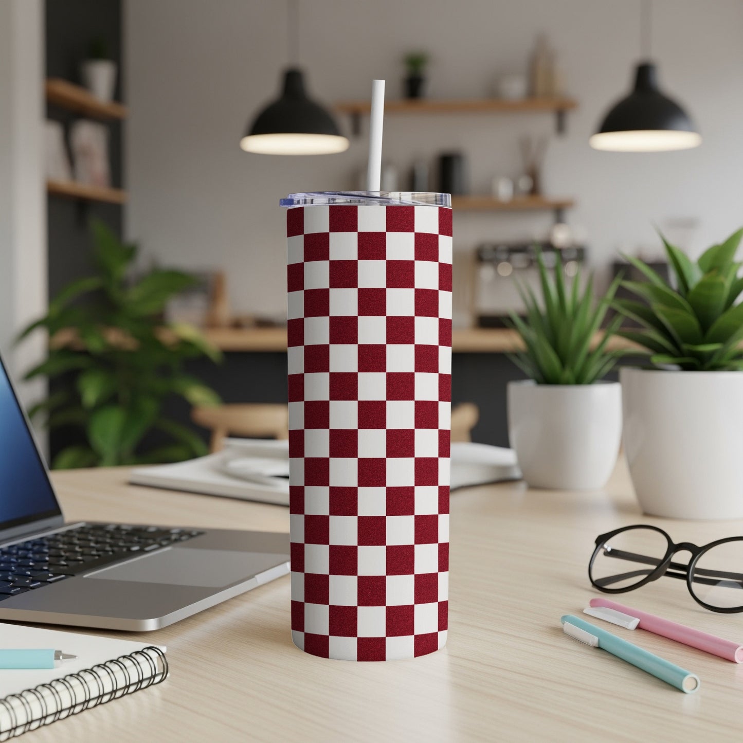 Maroon and white checkerboard pattern insulated tumbler with straw on desk.