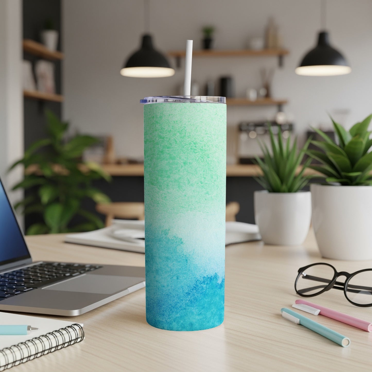 Tall tumbler with blue and green watercolor design on a desk.