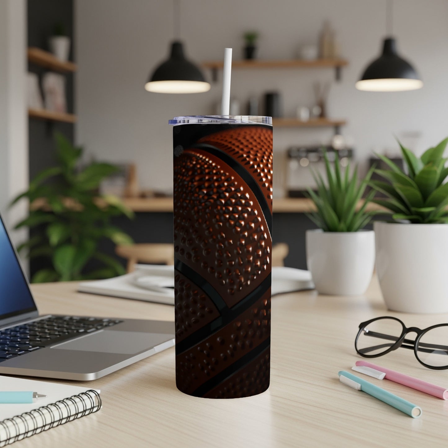Basketball tumbler with straw on a desk with a laptop and pens.