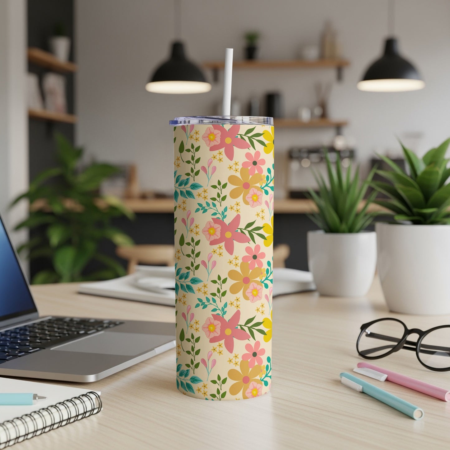 Floral patterned tumbler with straw on a desk next to a laptop.