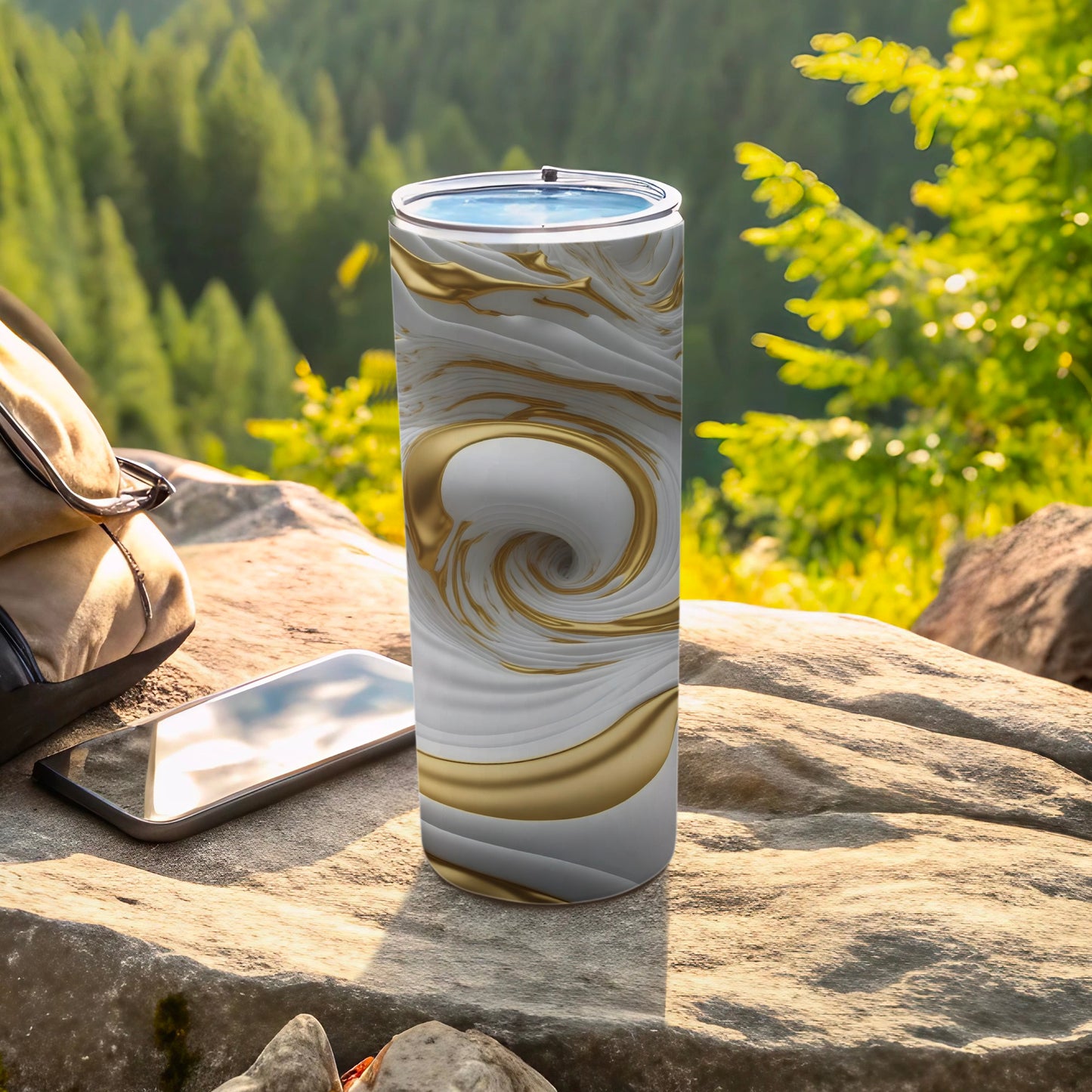 White and gold swirled tumbler on rock with phone and backpack.