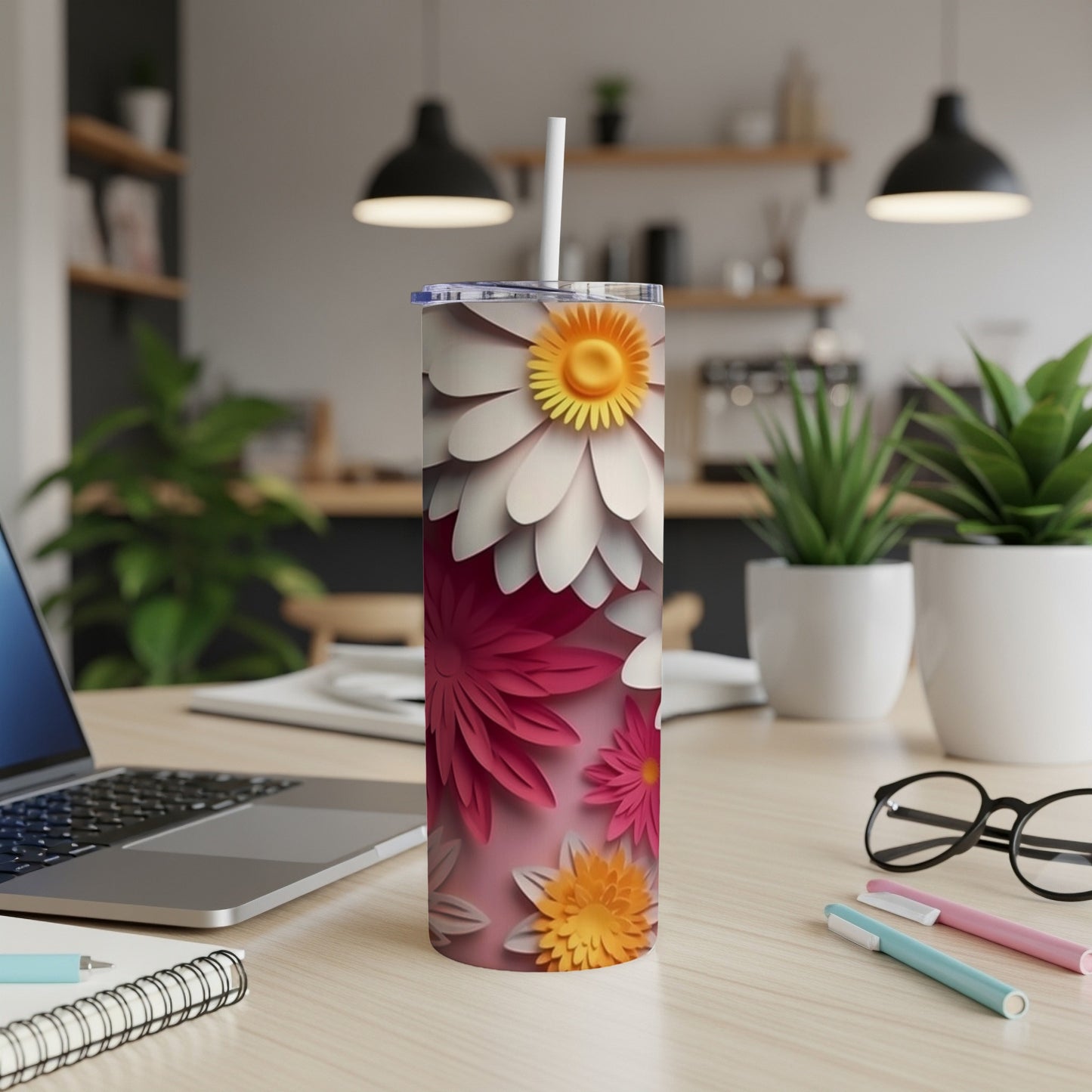Pink floral tumbler with straw on a wooden desk next to a laptop.
