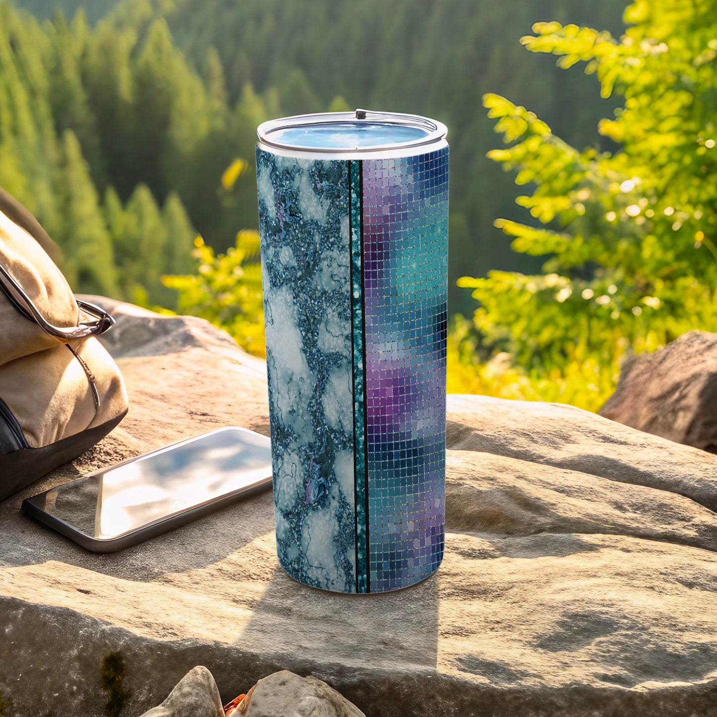 Patterned tumbler with marble and mosaic designs rests on rock next to phone.
