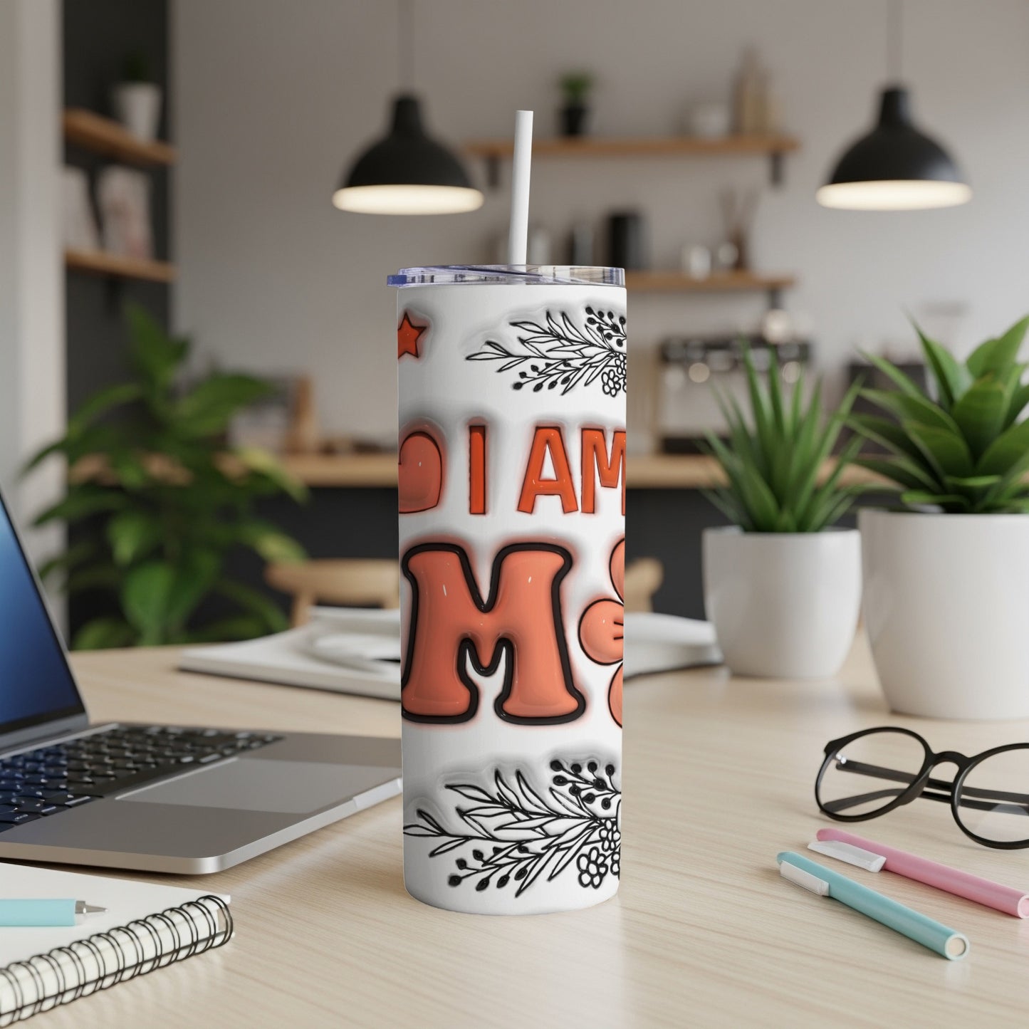 White tumbler with "I AM MOM" text and floral accents on a desk.