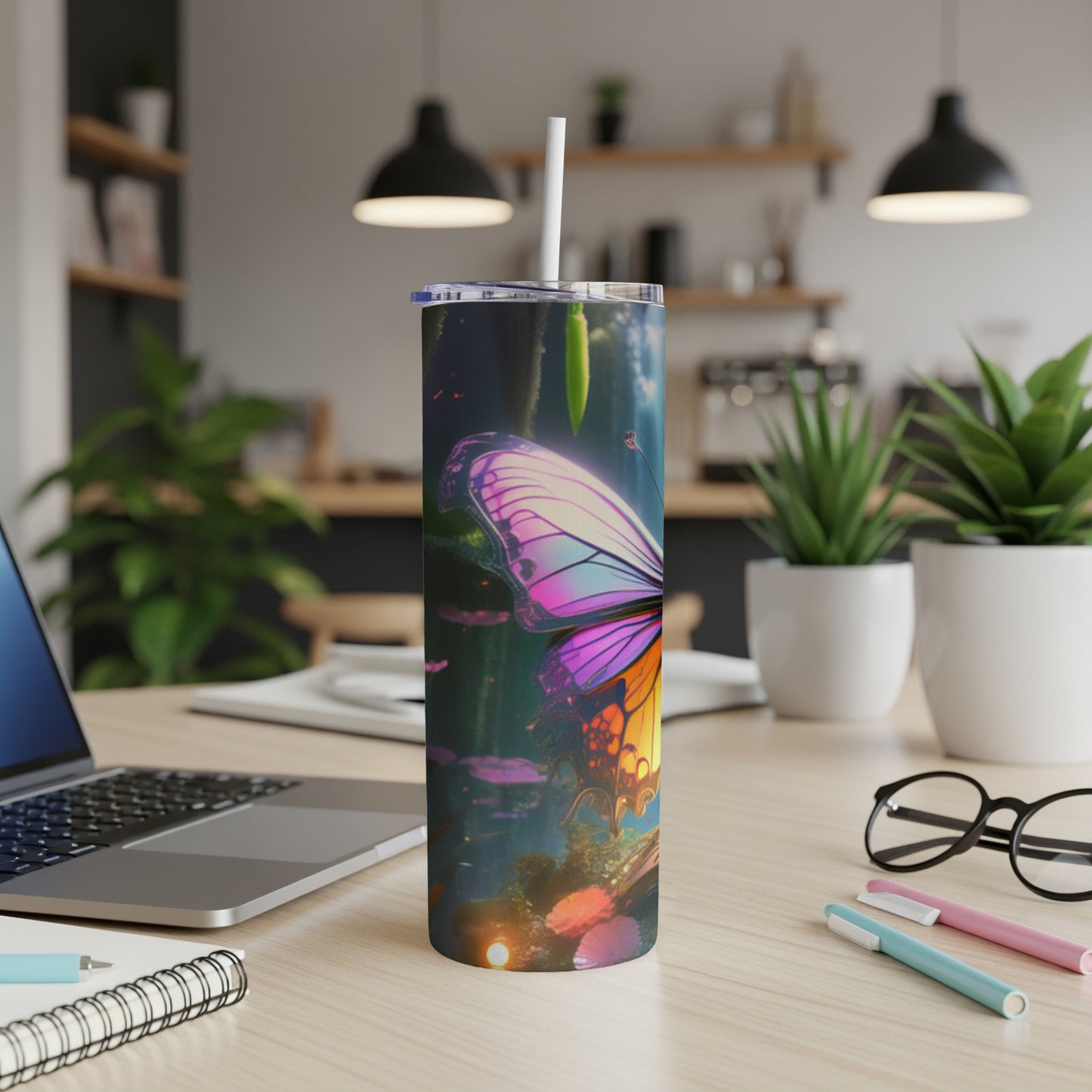 Butterfly tumbler with a straw on a desk with a laptop and pens.