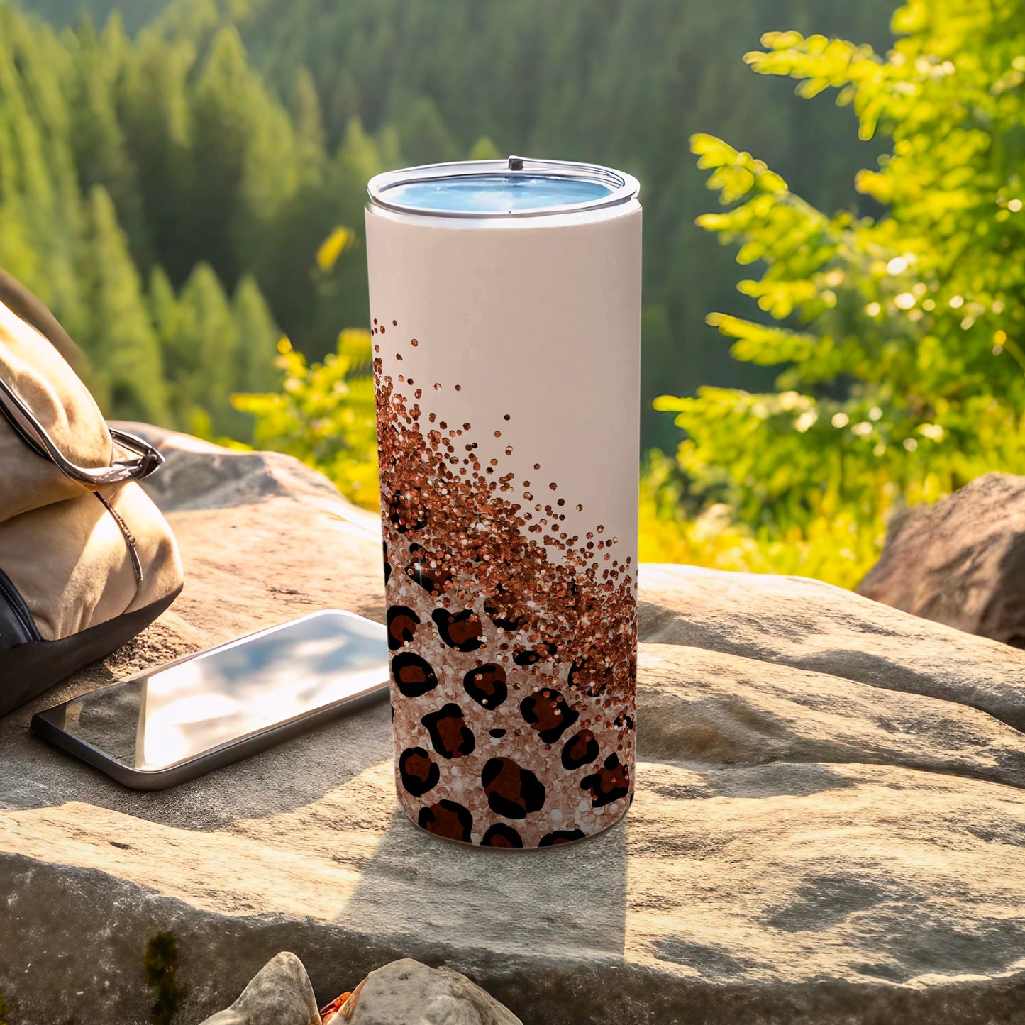 Sparkling leopard print tumbler on a rock with a backpack and phone.