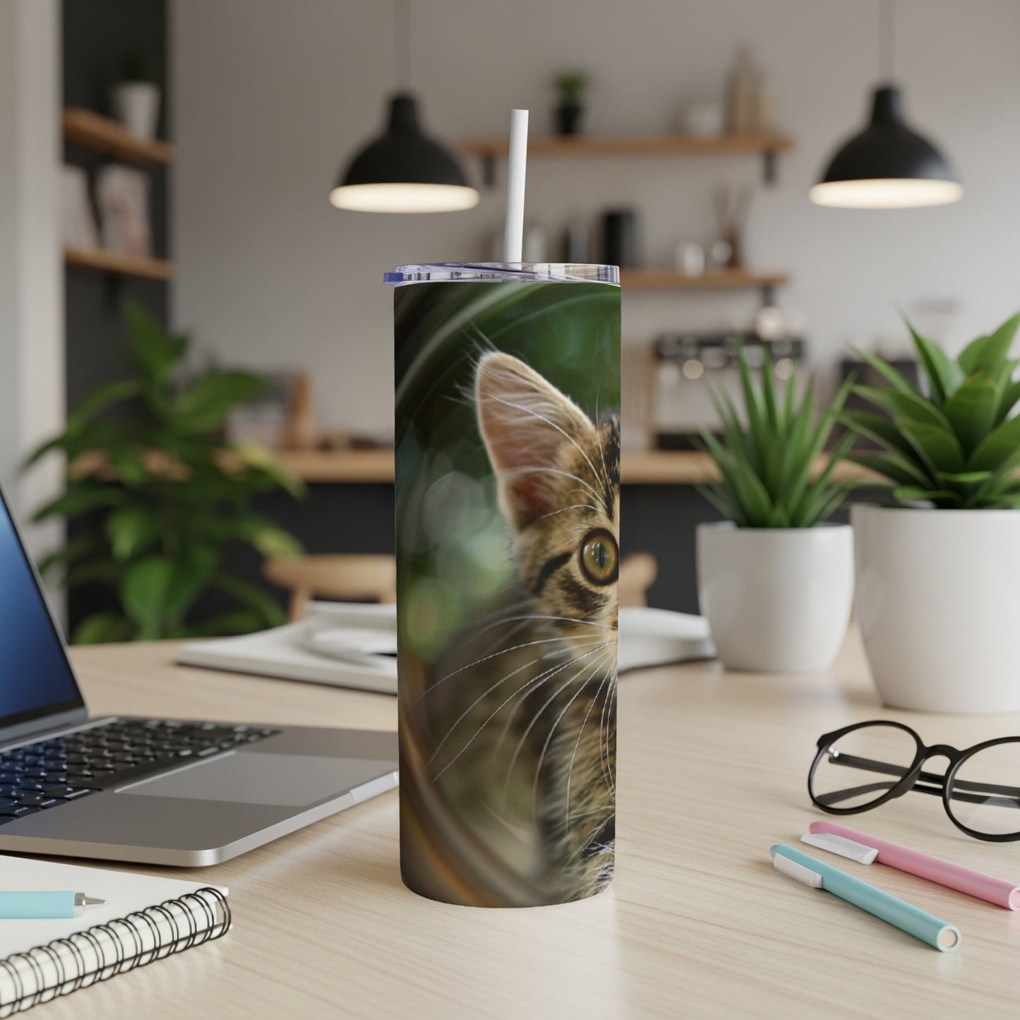 Close-up of a tabby kitten's face on a patterned tumbler with a straw.