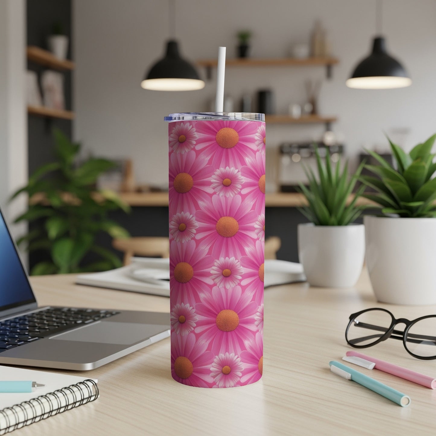 Pink floral tumbler with a straw on a desk with a laptop and pens.