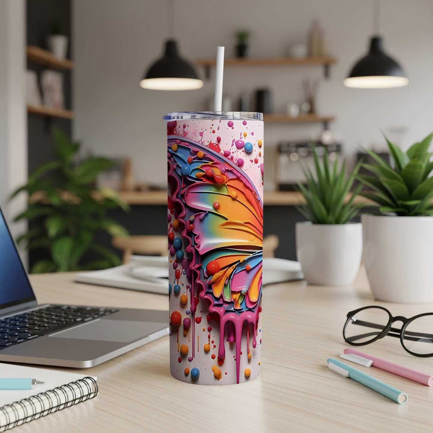 Dripping rainbow butterfly tumbler with straw on a desk.