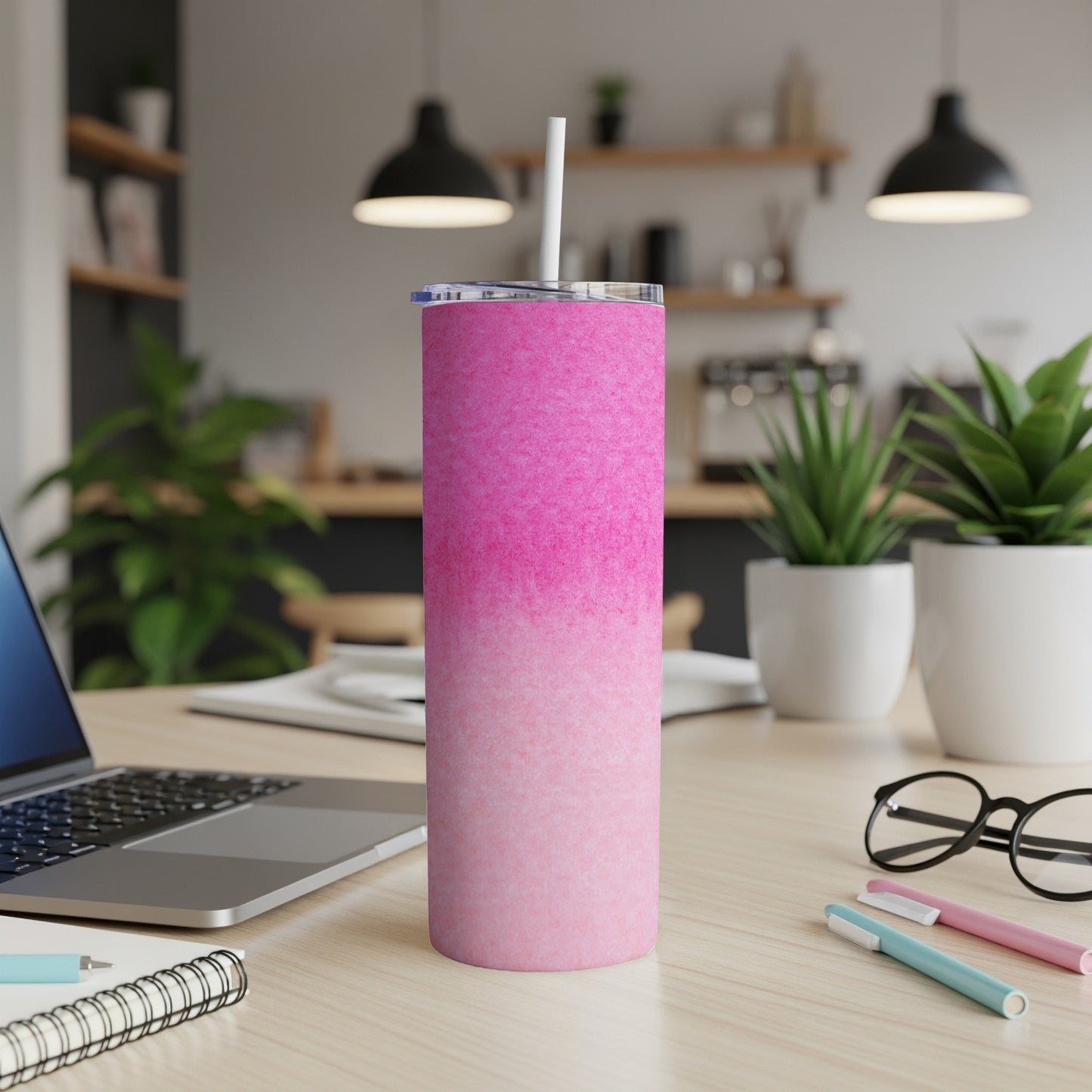 Pink gradient tumbler with straw on a desk with laptop and pens.