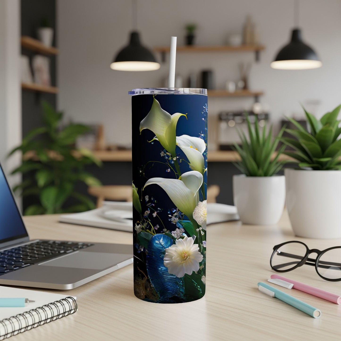 White calla lilies and green leaves on a dark blue tumbler with a straw.