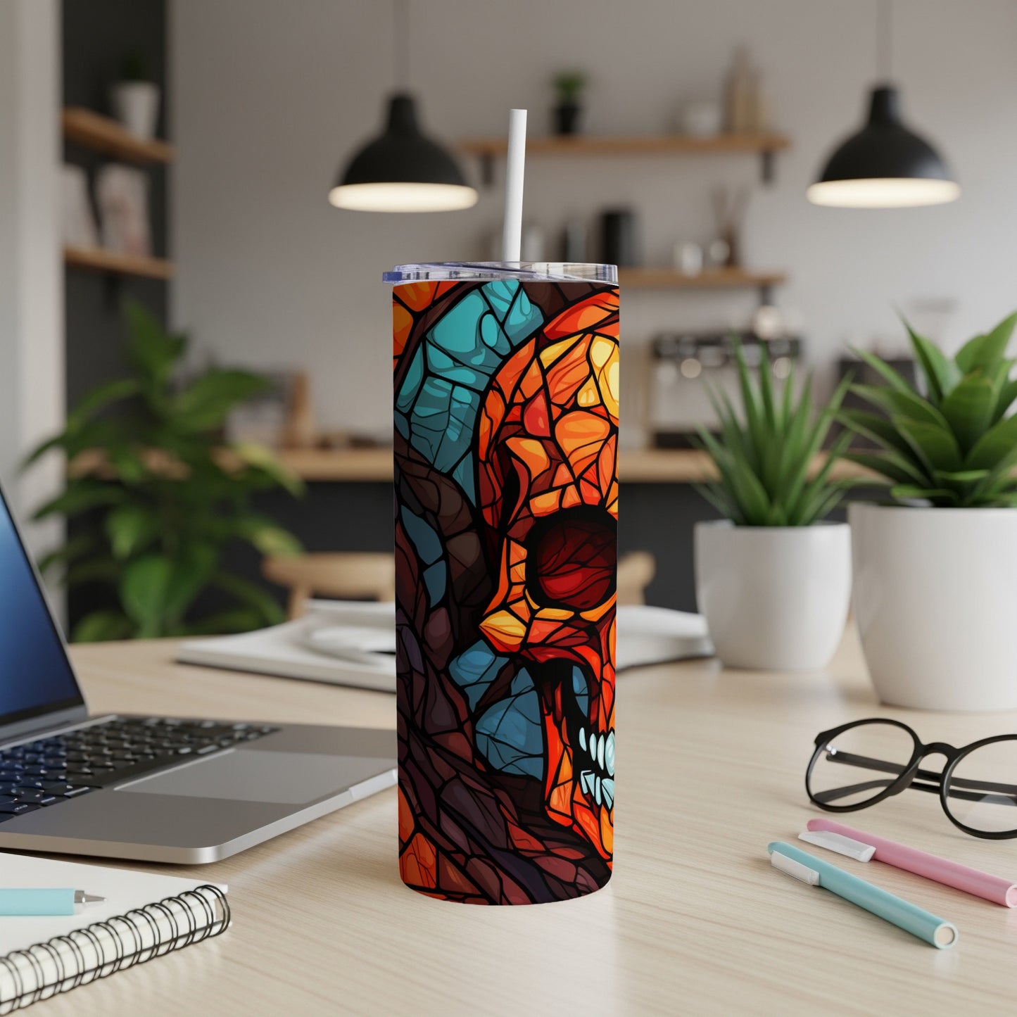 Stained glass skull tumbler with straw on a desk next to a laptop.