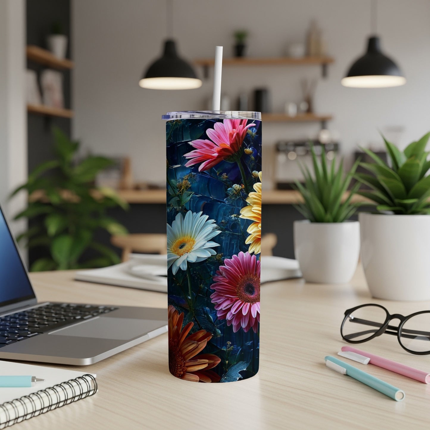 Floral tumbler with straw on a desk with a laptop and pens.